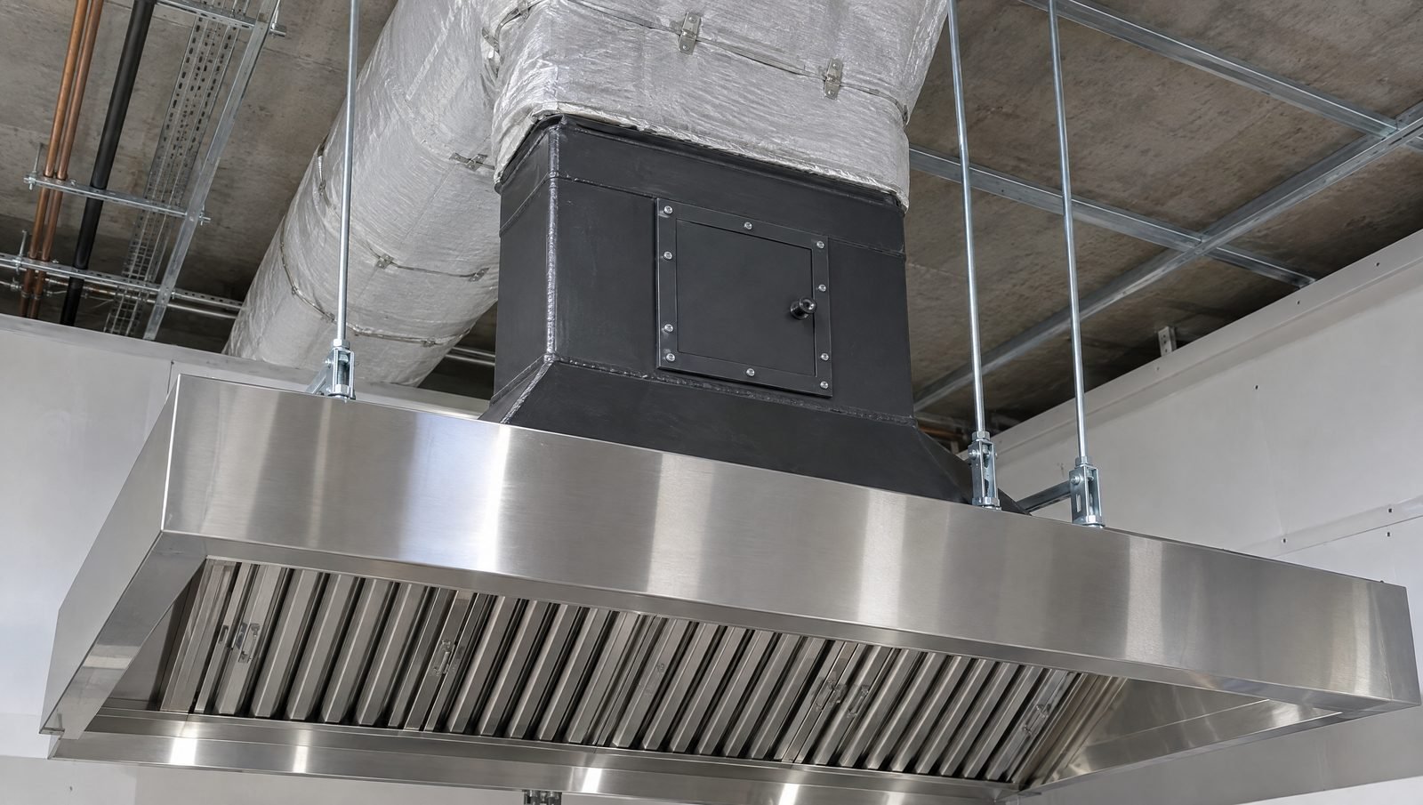 A stainless kitchen extract hood with baffle filters and a welded grease duct rising above it