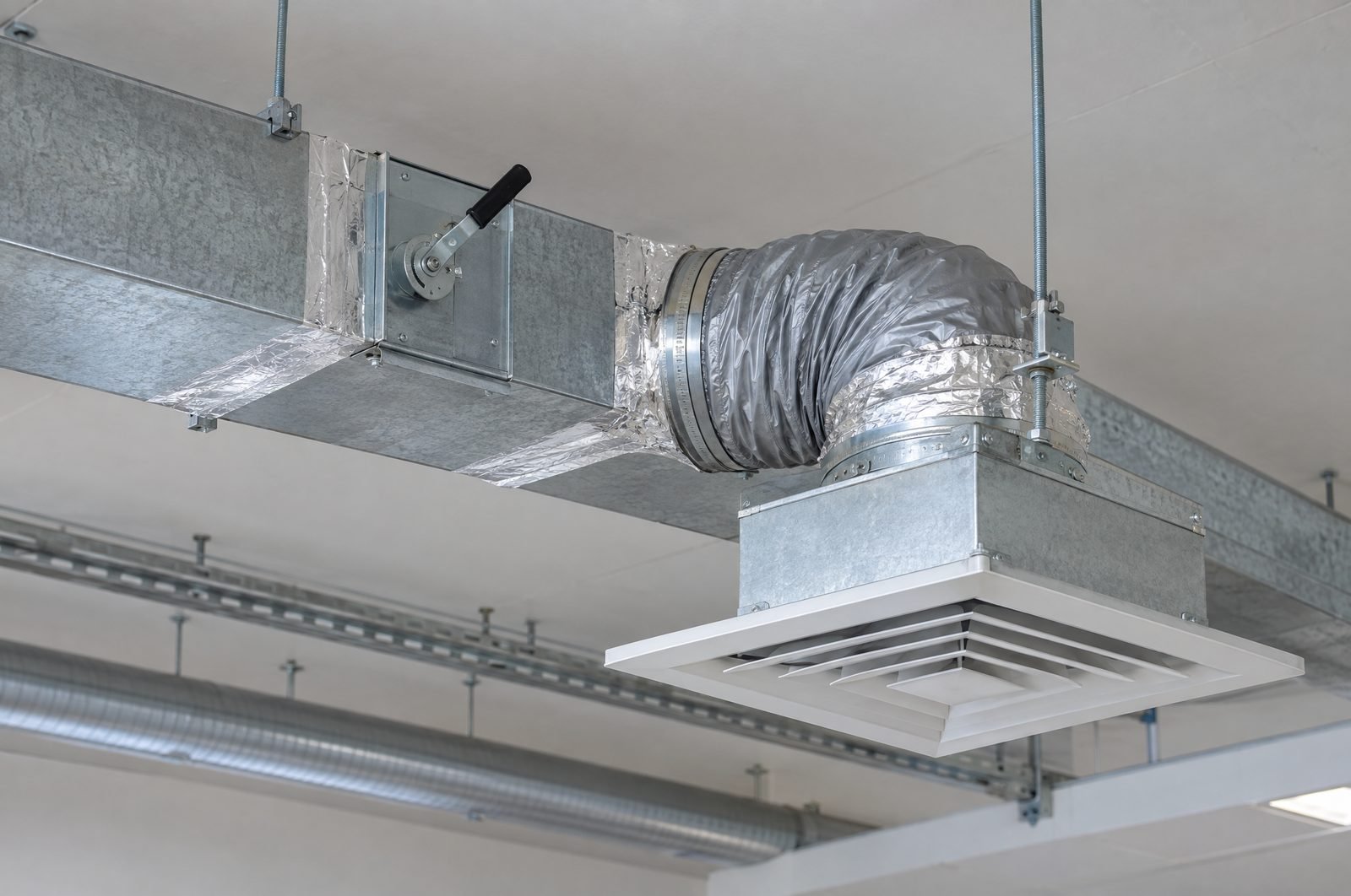 A galvanised duct connected to a square ceiling diffuser above the ceiling